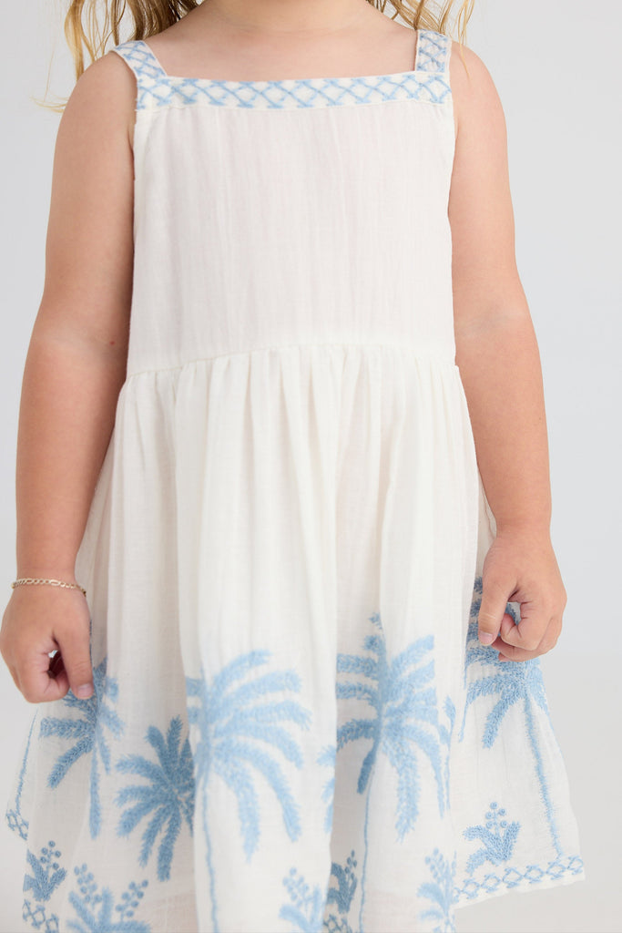 Child wearing a white dress with blue floral patterns on a plain background