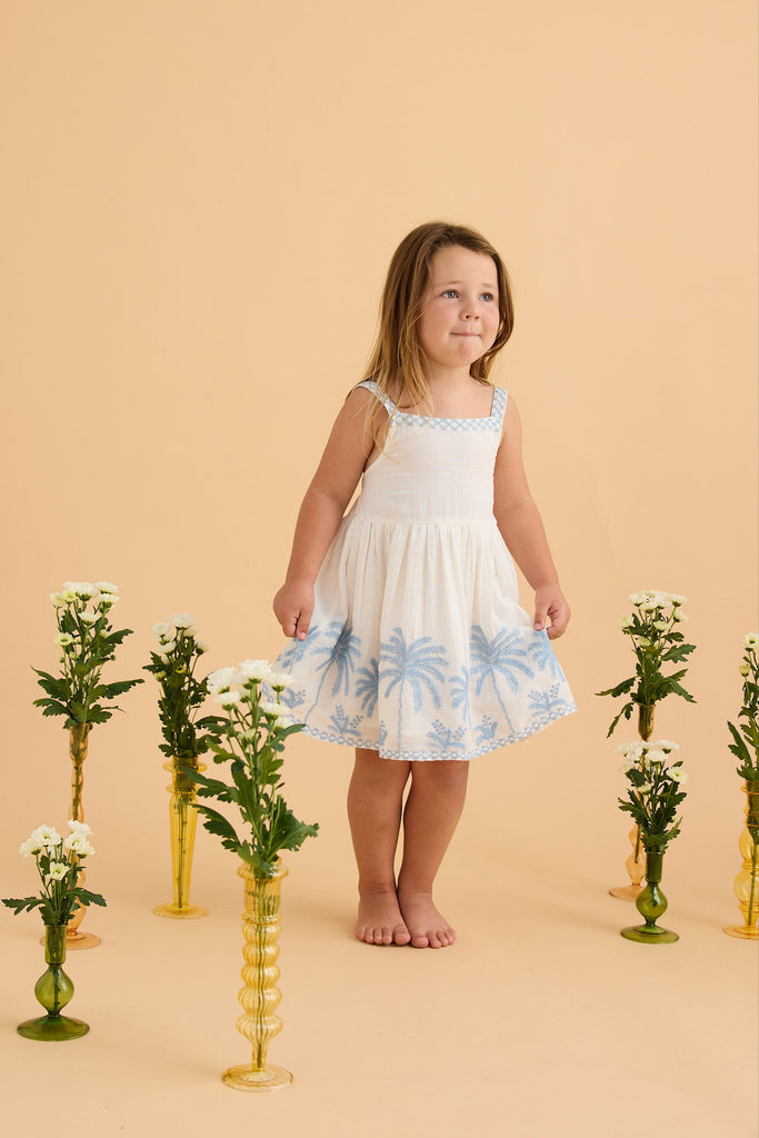 Young girl in a white dress standing among decorative plants on a beige background