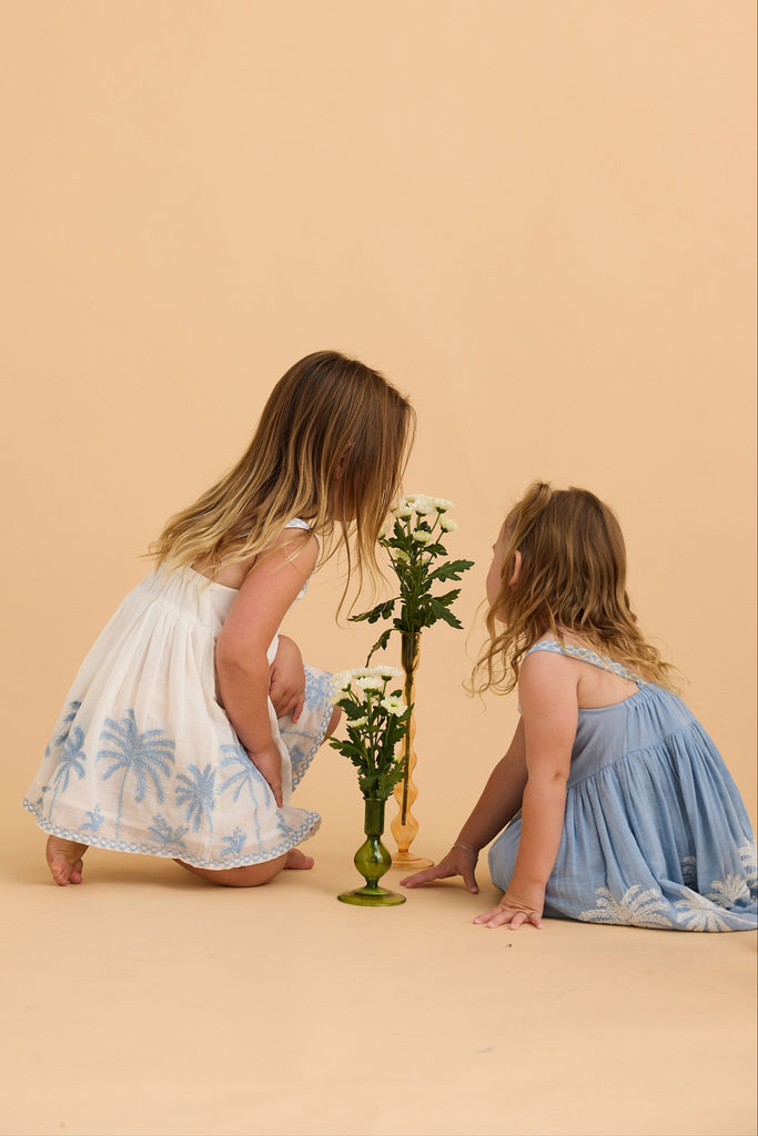Two young girls in floral dresses interacting with flower arrangements on a beige background