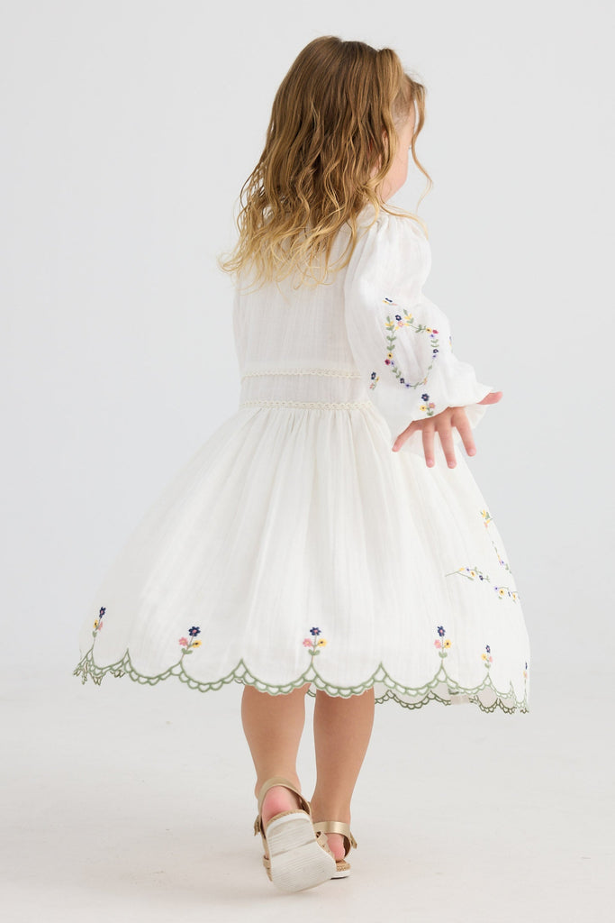 Young girl wearing a white dress with floral embroidery on a white background