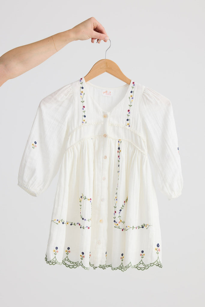 White embroidered blouse on a wooden hanger against a white background