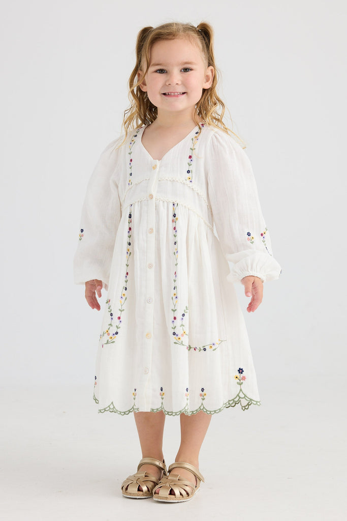 Young girl wearing a white dress with floral embroidery on a white background