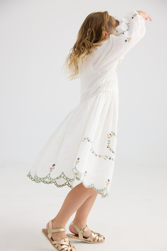 Young girl wearing a white dress with floral embroidery on a plain background