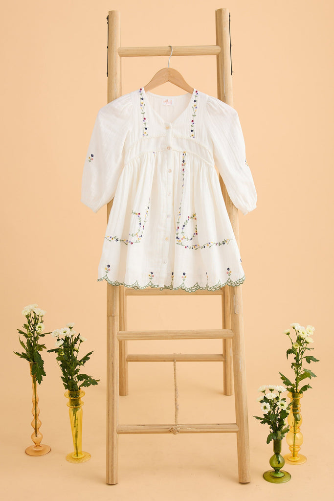 White embroidered dress on a wooden ladder with decorative vases on a beige background